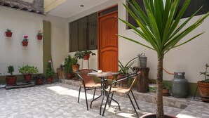 A patio with a round table and two wicker chairs, surrounded by potted plants and a palm tree. - Ruinas: Spacious 2-bedroom apartment in San Blas market area. Big kitchen! (Cusco)