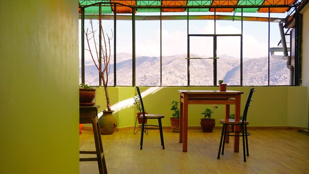 A room with a wooden floor, a table, two chairs, and potted plants. - Ruinas: Spacious 2-bedroom apartment in San Blas market area. Big kitchen! (Cusco)