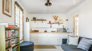 Una sala de estar acogedora con sofá, estantería y una zona de cocina con armarios blancos y encimera.