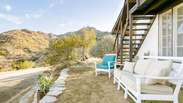 Un patio con un sofá blanco y una silla azul, rodeado por un borde de piedra y plantas en macetas.