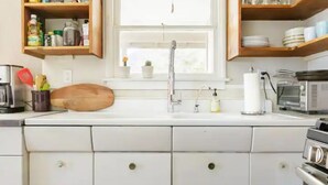 Una cocina con armarios blancos, una tabla de cortar de madera, un lavamanos de acero inoxidable y un tostador.