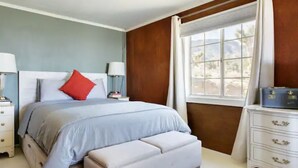 Un dormitorio con cama, mesitas de noche, cómoda y una ventana con cortinas.