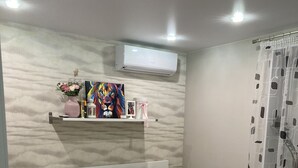 Quarto com cama, berço, ar condicionado fixado na parede, prateleira com objetos decorativos e janela com cortina.