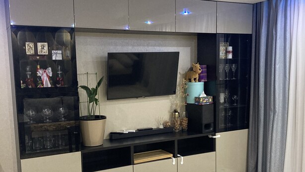 Uma sala de estar moderna com uma televisão de tela grande montada em um móvel, uma planta em vaso e uma mesa pequena.