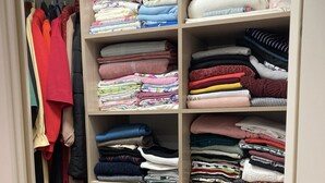 Um armário bem organizado com várias prateleiras e gavetas, contendo roupas dobradas e cobertores arrumados.