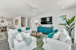 A modern living room with white sofas, a teal cabinet, and a large TV.