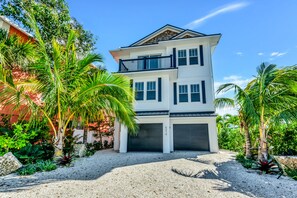 A two-story house with a balcony, a garage, and a well-maintained garden with palm trees and other plants.