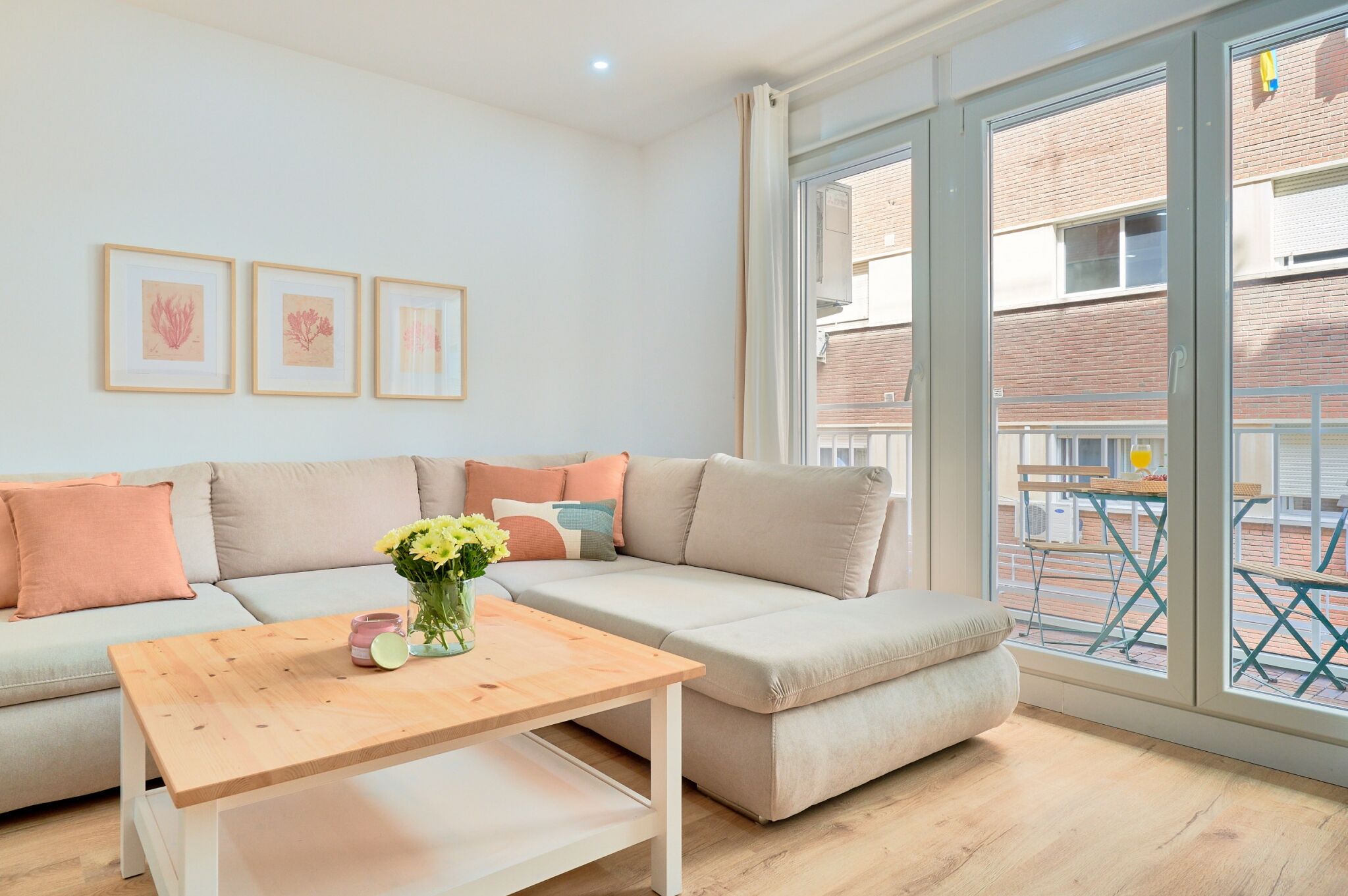 Ein modernes Wohnzimmer mit einem Ecksofa, einem Holztisch und einem großen Fenster mit Blick auf ein Backsteingebäude.