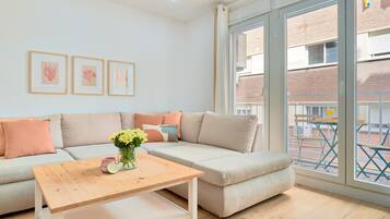 Ein modernes Wohnzimmer mit einem Ecksofa, einem Holztisch und einem großen Fenster mit Blick auf ein Backsteingebäude.