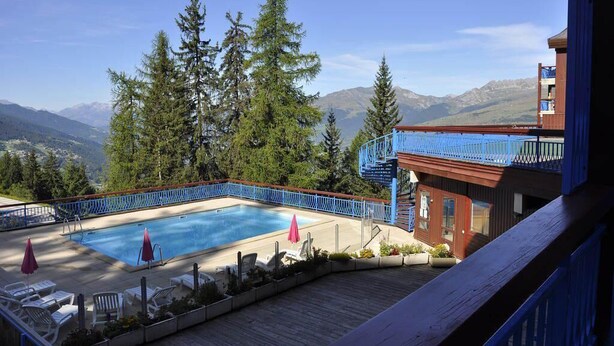 A pool area with a view of mountains, surrounded by trees and a wooden deck. - 100m from resort center, 8th floor, balcony, tv, 30m², Les Arcs (Les Arcs)