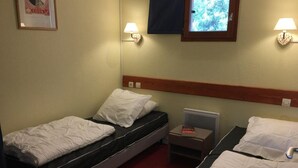 A hotel room with two single beds, a small table with a book, a nightstand, and a window with a view of trees. - 100m from resort center, 8th floor, balcony, tv, 30m², Les Arcs (Les Arcs)