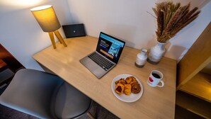 A wooden desk with a laptop, a plate of pastries, a coffee cup, a lamp, and decorative vases. - Charming 2-bed Apartment in Windsor - Free Parking (Windsor)