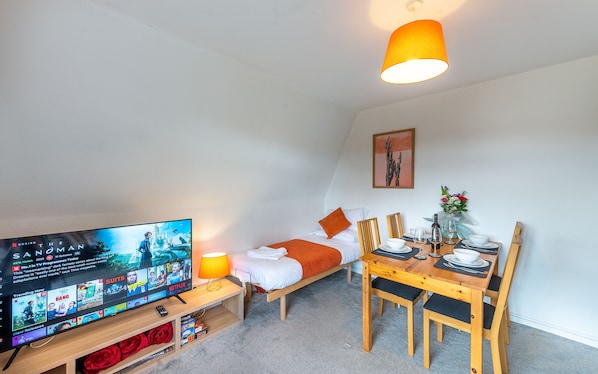 Een gezellige kamer met een bed, een televisie, een eettafel met stoelen en een lamp.