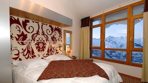 Ein Hotelzimmer mit einem grossen Bett, einem verzierten Kopfteil, einem Nachttisch, einer Lampe und einem Fenster mit Bergblick.