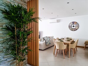 A modern dining area with a wooden table set for four, a large wall clock, and a bamboo plant.
