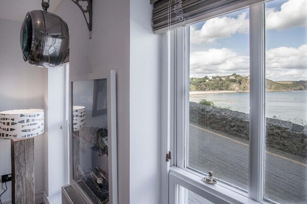 Een kamer met een groot raam met uitzicht op de kust, een lamp met vismotief en een spiegel met een geometrisch ontwerp.
