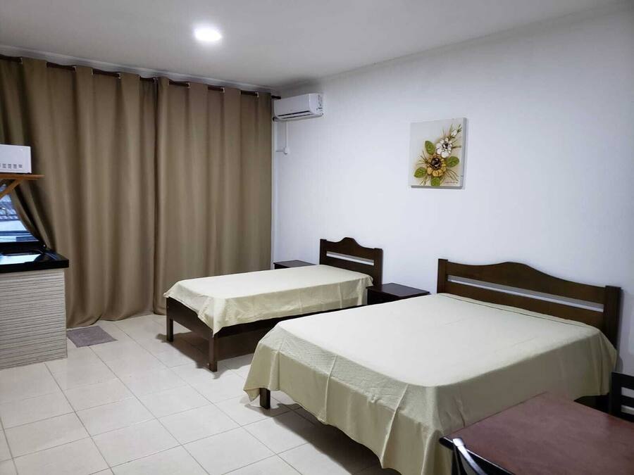 Habitación de hotel con dos camas individuales, un escritorio, una silla, un ventanal con cortinas, un equipo de aire acondicionado y un cuadro en la pared.