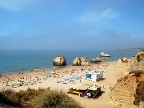 A beach with large rock formations, a sandy shore, and beach umbrellas. - Larimar Orange Apartment, Portimão, Algarve !new! (Portimão)