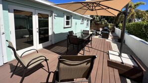 Une terrasse extérieure couverte, équipée d’une table et de chaises, d’un barbecue et d’un grand parasol.