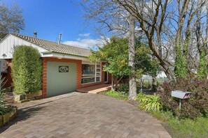 A residential house with a paved driveway, a garage, and a well-maintained garden with various plants and trees.