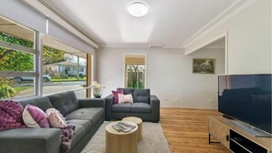 A modern living room with a large window, a grey sofa, a smaller sofa, a coffee table, and a TV. - Collwood Cottage. Four Beds + Fireplace. Orange. (Orange)
