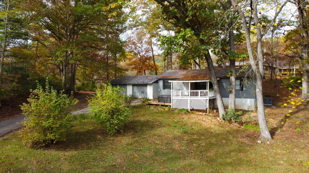 A single-story house with a porch, surrounded by trees and a grassy yard.