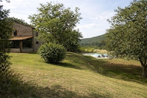 A stone house with a covered patio, a swimming pool, and a grassy area with trees.
