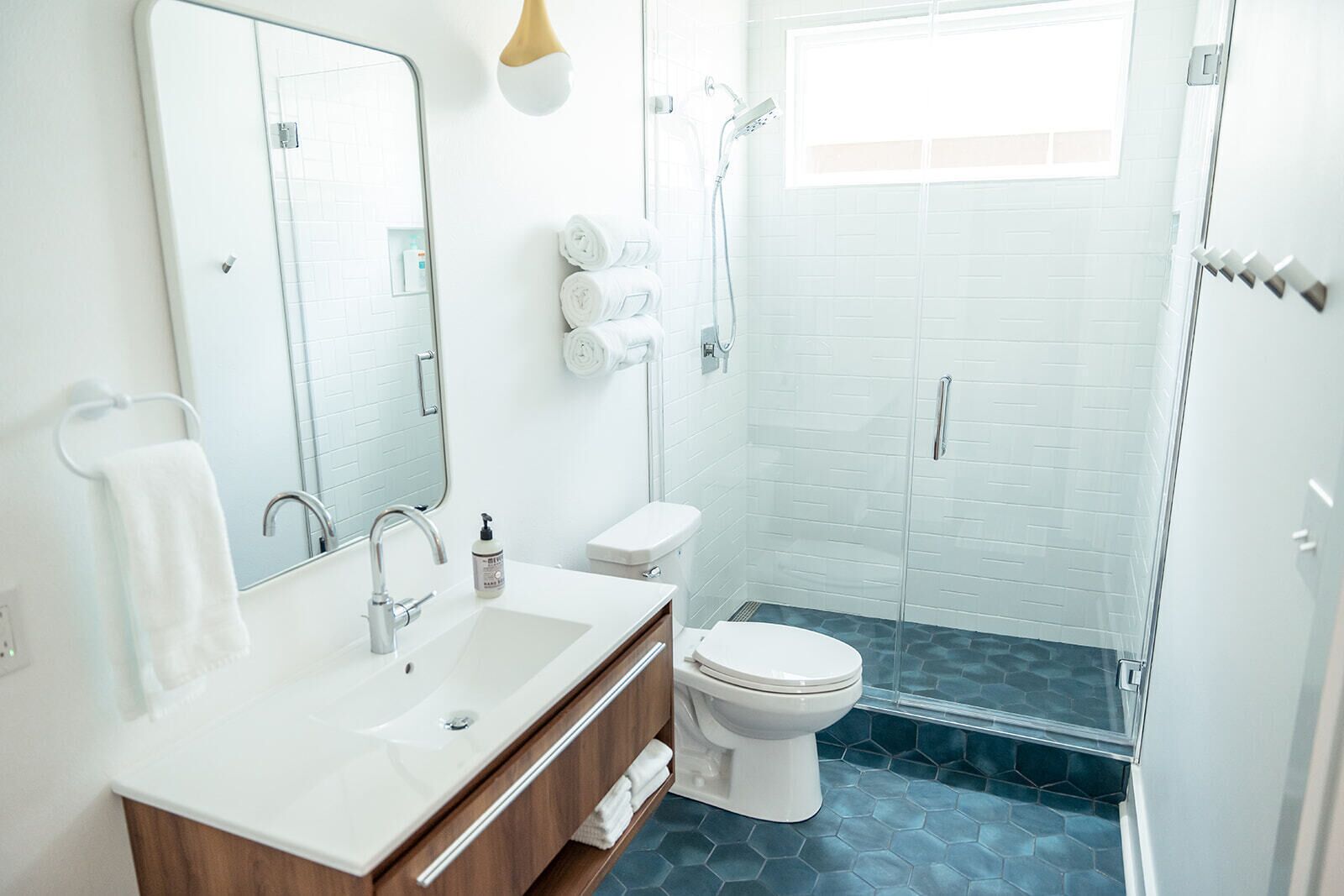 Un bagno moderno con lavandino, specchio e servizi igienici bianchi. È presente un box doccia in vetro e un portasciugamani con asciugamani.