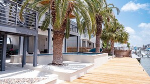 Ein Hotel am Wasser mit Holzterrasse, Palmen und einem Poolbereich.