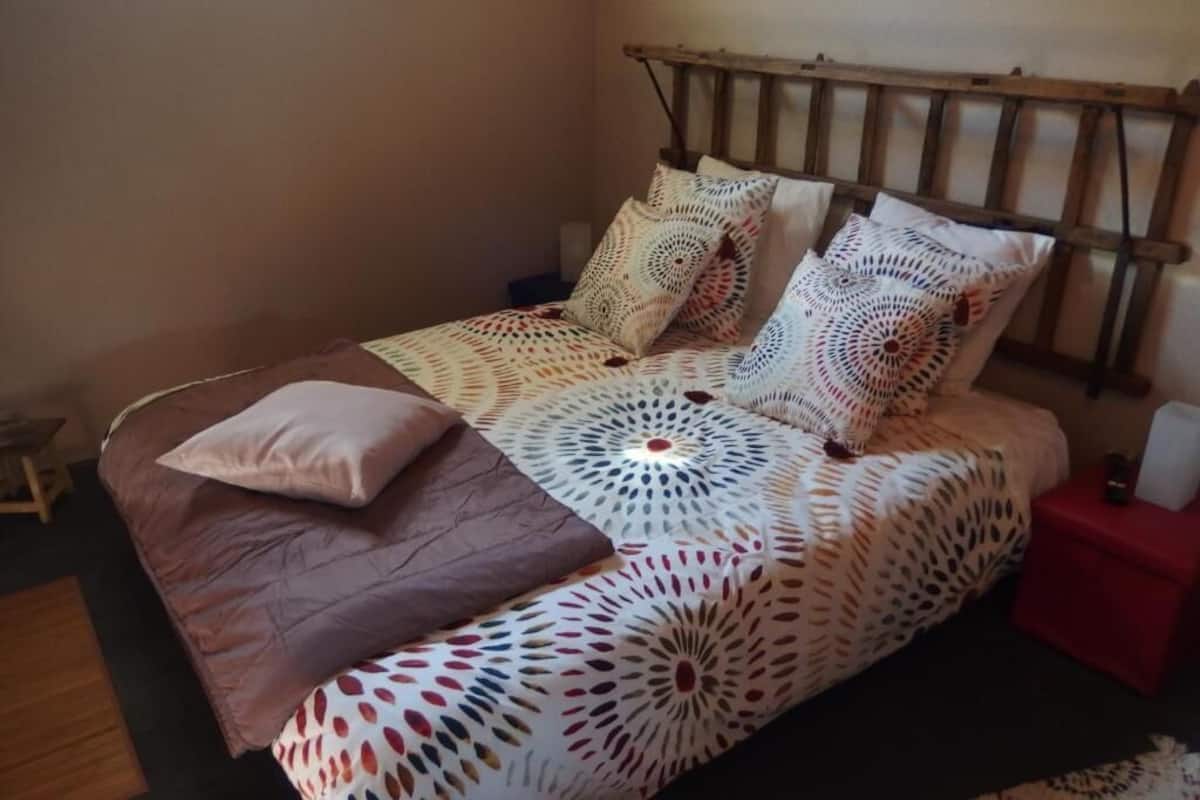 A bed with a patterned bedspread, multiple pillows, and a wooden headboard.
