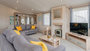 Ein modernes Wohnzimmer mit einem grauen Sofa, gelben Kissen, einem Holztisch, einem Fernseher und einem Kamin.