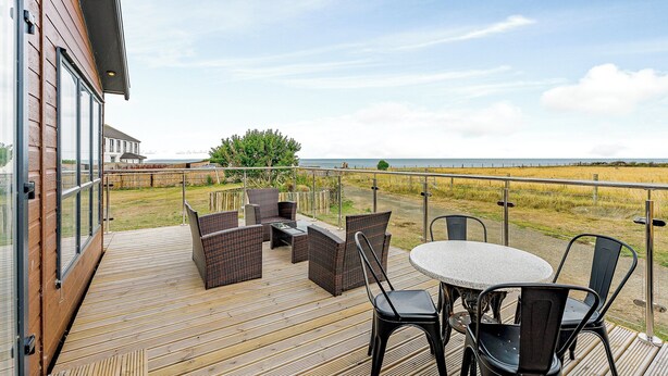 Eine Holzterrasse mit Gartenmöbeln, Blick auf das Meer und einer Rasenfläche.