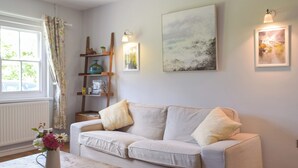 A living room with a sofa, a coffee table, a vase with flowers, a bookshelf, and wall-mounted lights.