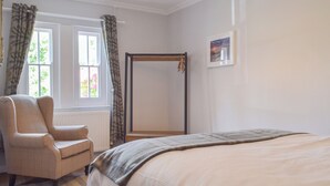 A bedroom with a bed, a chair, a window with curtains, a radiator, and a framed picture on the wall.