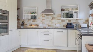 A modern kitchen with white cabinets, a built-in oven, a range hood, and a tiled backsplash.