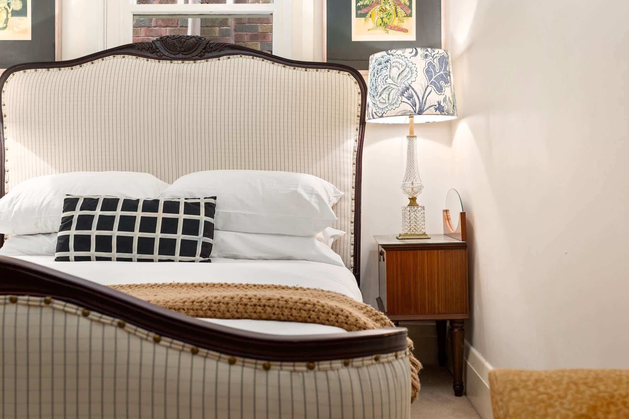 A neatly made bed with a striped headboard, a patterned pillow, and a bedside lamp on a wooden nightstand.