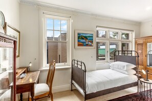 A bedroom with a bed, a desk, a chair, and a window with a view of buildings. - Eclectic Art Deco Apartment in great location (Potts Point)