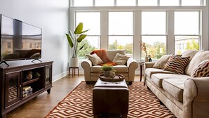 Uma sala de estar com sofá, poltronas, mesa de centro e televisão sobre um suporte.