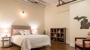 Quarto com cama grande, luminárias de cabeceira, estante de madeira e uma cadeira.