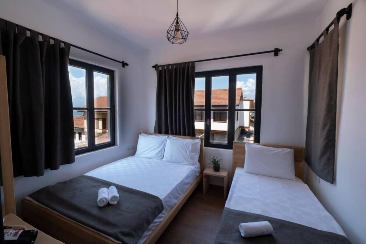 Une chambre d’hôtel avec deux lits simples, une petite table de chevet agrémentée d’une plante et de grandes fenêtres avec des rideaux.