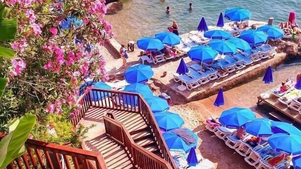 A beach with clear blue water, sun loungers, and blue umbrellas. - Solo Boutique Hotel (Antalya)