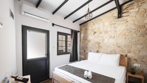 A bedroom with a stone wall, a bed with white linens, a wooden bench, and a small table with fruits and a bottle. - Solo Boutique Hotel (Antalya)