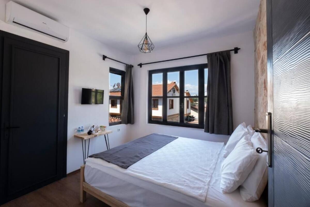 Une chambre à coucher avec un lit, une petite table sur laquelle se trouvent divers objets, un téléviseur et une fenêtre avec des rideaux.