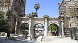 An ancient stone archway with columns, leading to a staircase and a view of a palm tree and a tower in the background. - Solo Boutique Hotel (Antalya)