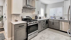 A modern kitchen with a stainless steel stove, oven, and dishwasher, light-colored cabinets, and a window with blinds. - Sauna- Hot Tub- Garage Game Room- Outdoor Dining (Arvada)