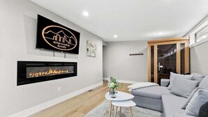 A modern living room with a fireplace, a grey sofa, a small coffee table, and a TV mounted on the wall. - Sauna- Hot Tub- Garage Game Room- Outdoor Dining (Arvada)