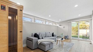 A modern living room with a grey sectional sofa, a small white table, and a wooden sauna. - Sauna- Hot Tub- Garage Game Room- Outdoor Dining (Arvada)