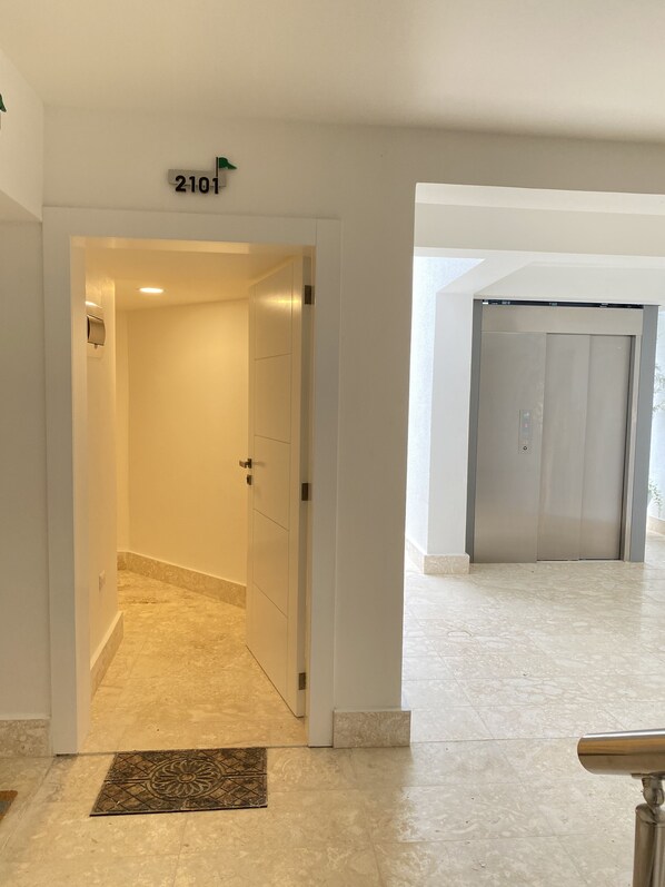 A hallway with a door marked "2101" leading to an elevator. The floor is tiled with a marble-like pattern.