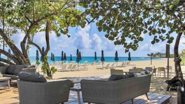 A beachside lounge with wicker furniture, umbrellas, and a view of the ocean.