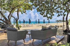 A beachside lounge with wicker furniture, umbrellas, and a view of the ocean.